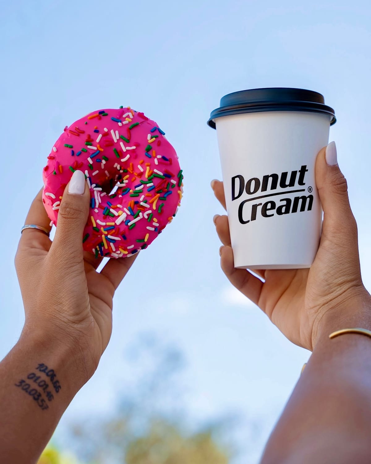 Hands holding a sprinkled donut and a branded coffee cup